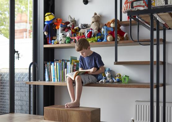 a boy sitting on a shelf reading a book