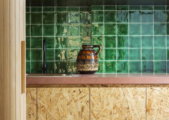 a green tile wall with a brown and black pitcher on top of it