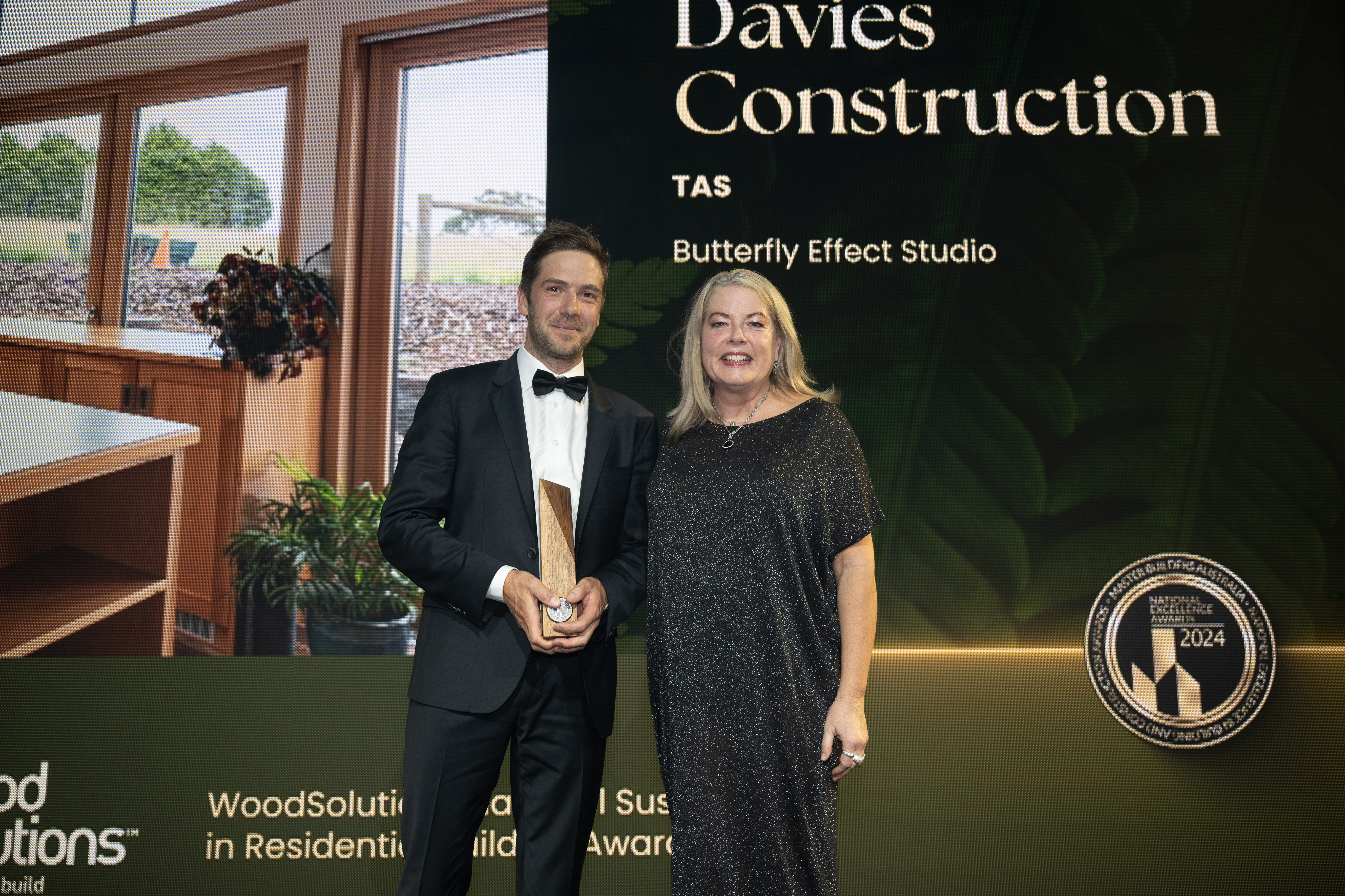 Man holding a wood trophy while a woman congratulates him.