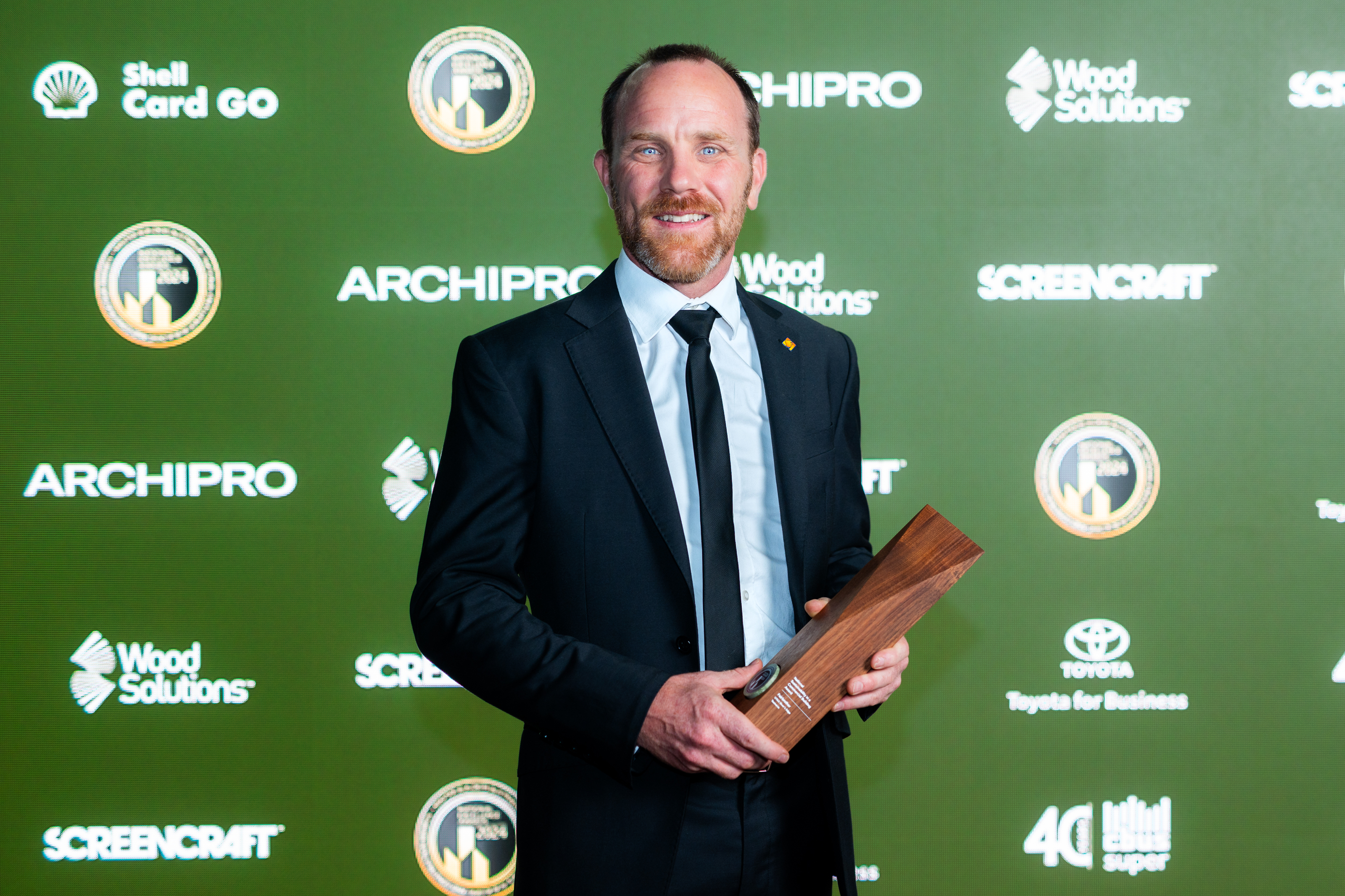 Man holding a wood trophy against a green media wall.