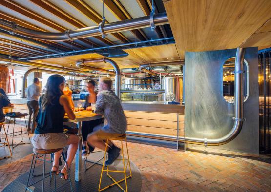 people sitting at a table in a room with pipes and a large metal structure