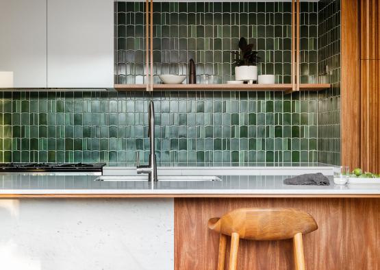 a kitchen with a stool and green tile wall