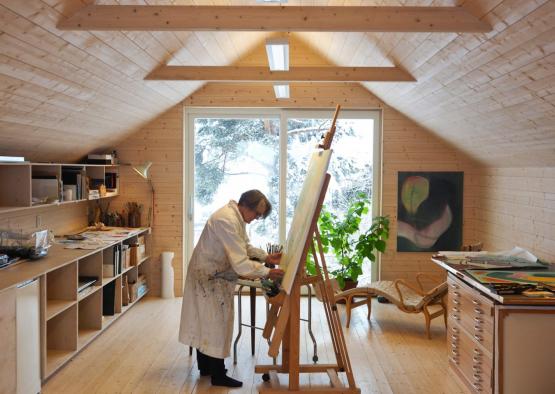 a man painting on a canvas in a room with a large window