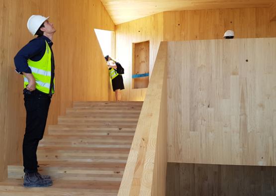 a man in a safety vest and helmet looking up at a wooden staircase